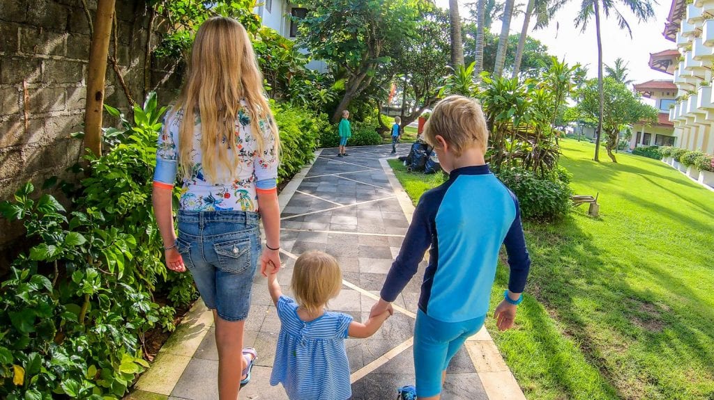 Lucy, Grace. and Grant walking on a sidewalk through palm trees holding hands 